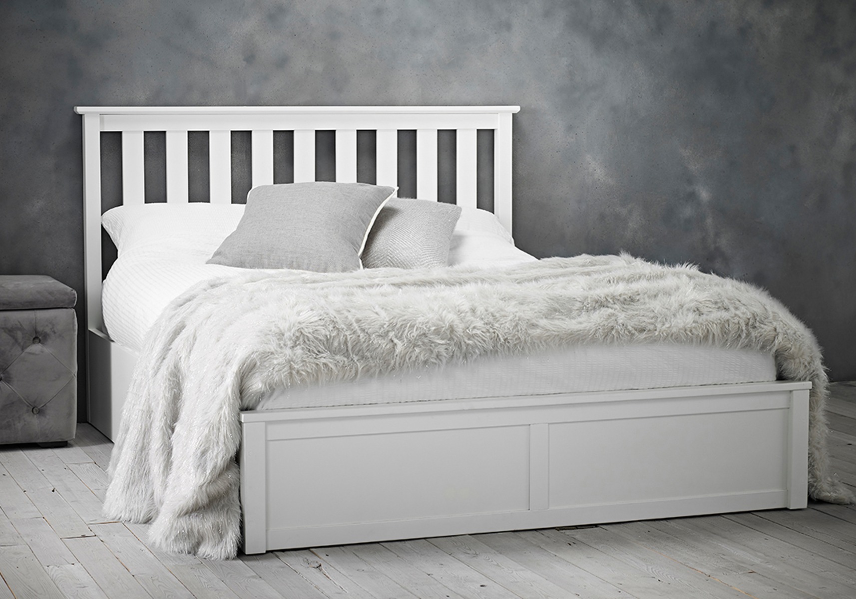 White wooden double bed against grey wall, with grey and white bedsheets